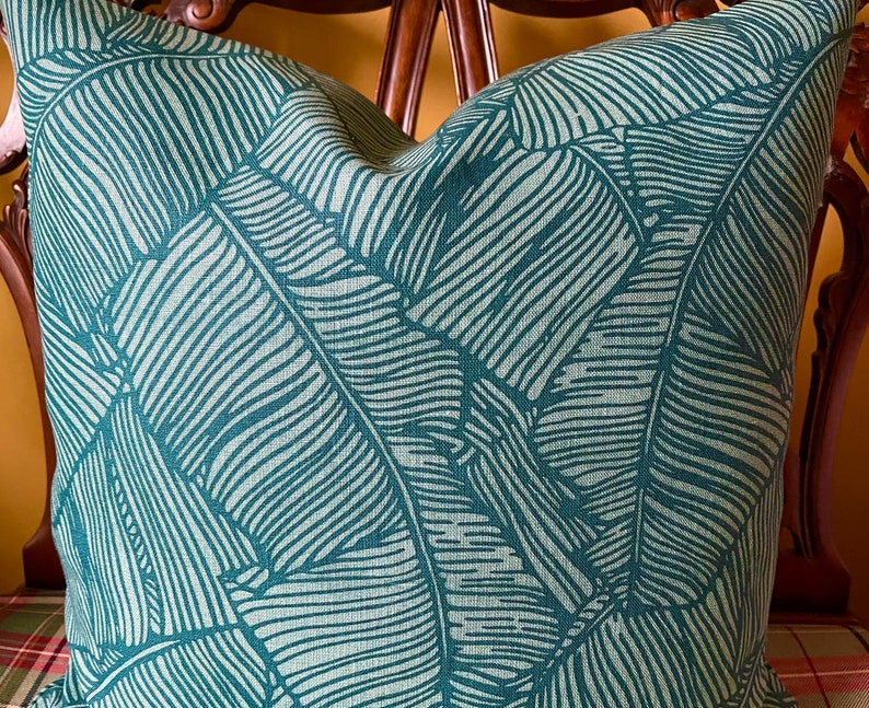May include: A teal green throw pillow with a white leaf pattern. The leaves are stylized and resemble banana leaves.
