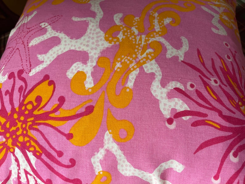 May include: Pink fabric with a white and orange floral pattern. The pattern features stylized flowers, coral, and starfish.