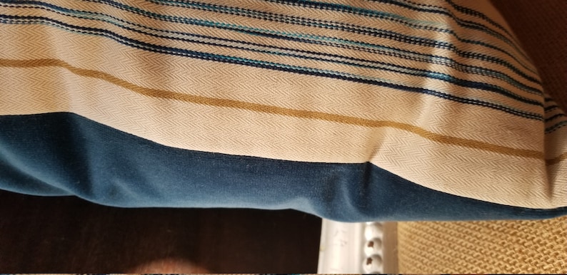 May include: A blue and white striped throw pillow with a gold stripe. The pillow is made of a soft, textured fabric.