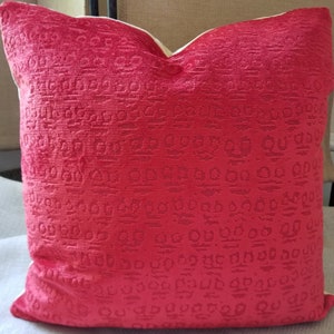 May include: Red velvet pillow with a textured pattern and a button detail. The pillow has a cream-colored border.