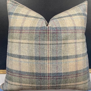 May include: Square decorative pillow with a plaid pattern in beige, blue, green, and burgundy. The pillow has a soft, textured appearance, and the plaid design is evenly spaced across the fabric. The pillow is likely used for home decor.