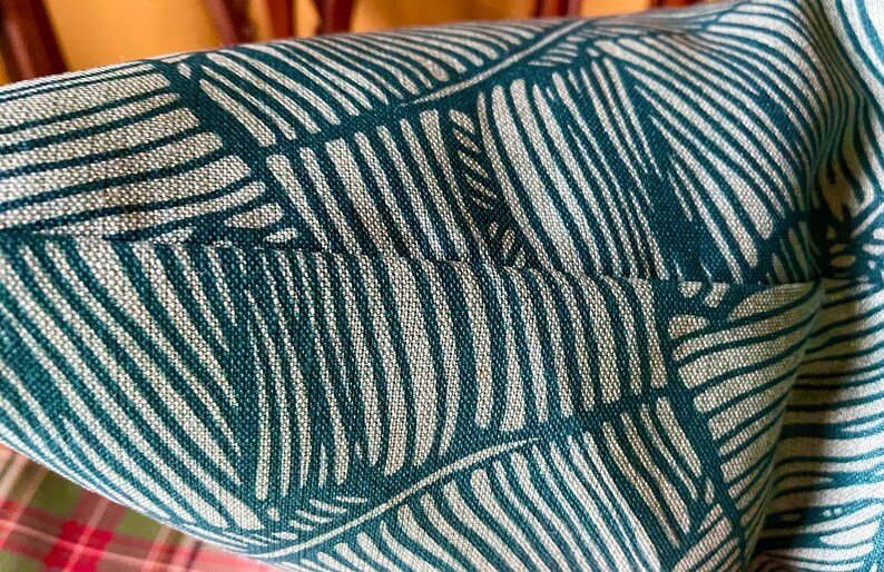May include: Close-up of a teal and white striped fabric with a leaf pattern. The fabric has a textured weave.