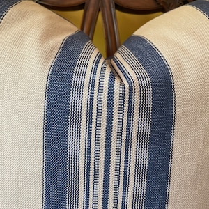 Puede incluir: Primer plano de una almohada a rayas con rayas azules y beige alternadas. La almohada est&aacute; hecha de una tela tejida con una textura sutil.