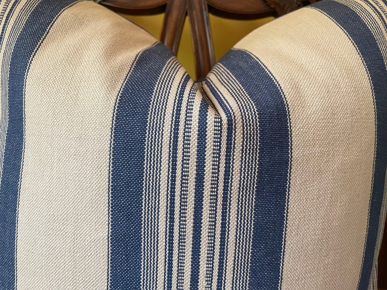 Puede incluir: Primer plano de una almohada a rayas con rayas azules y beige alternadas. La almohada est&aacute; hecha de una tela tejida con una textura sutil.