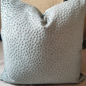 May include: A soft, light blue throw pillow with a textured, pebble-like pattern.