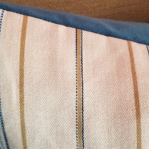 May include: A close-up of a striped pillow with a herringbone pattern. The pillow is made of a soft, textured fabric with blue, white, and gold stripes.