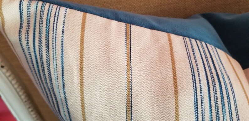 May include: A close-up of a striped pillow with a herringbone pattern. The pillow is made of a soft, textured fabric with blue, white, and gold stripes.