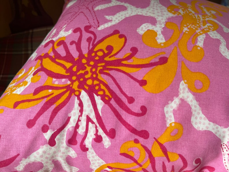 May include: Pink fabric with a floral pattern in shades of orange, yellow, and pink. The pattern features stylized flowers and coral.