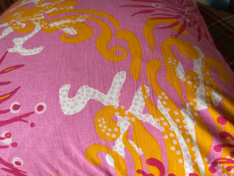 May include: Pink fabric with a yellow and white floral pattern. The fabric has a textured surface and a subtle sheen.