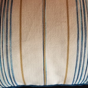 May include: A white pillow with blue and gold stripes. The pillow is made of a soft, textured fabric.