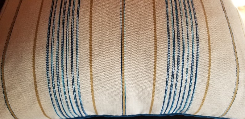 May include: A white pillow with blue and gold stripes. The pillow is made of a soft, textured fabric.