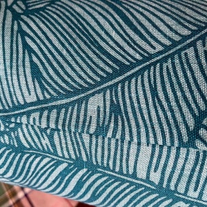 May include: Close-up of teal blue fabric with a white leaf pattern. The fabric has a textured, woven look.