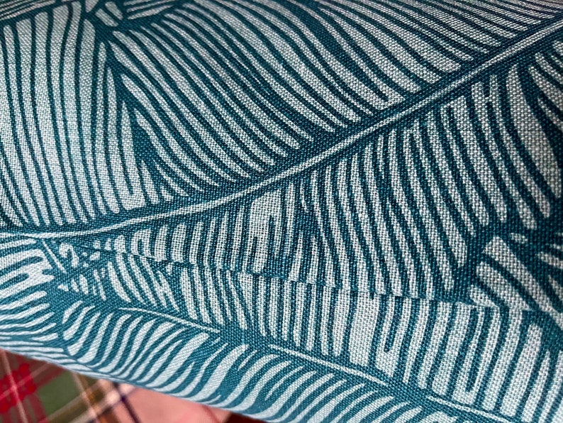 May include: Close-up of teal blue fabric with a white leaf pattern. The fabric has a textured, woven look.