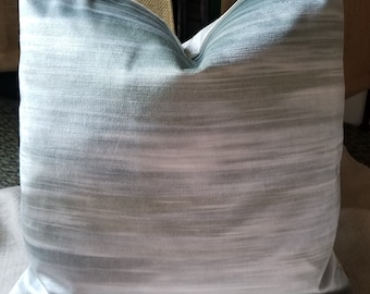 Puede incluir: Una almohada suave de rayas blancas y azules claras con un sutil efecto degradado. La almohada está hecha de una tela suave y sedosa.