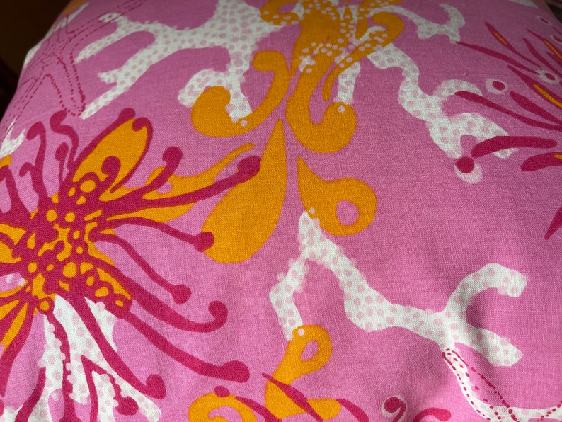 May include: Pink fabric with a floral pattern in shades of orange and pink. The pattern features stylized flowers, coral, and sea life.