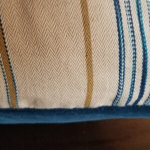 May include: A beige and blue striped throw pillow with a zipper closure and a blue velvet trim.