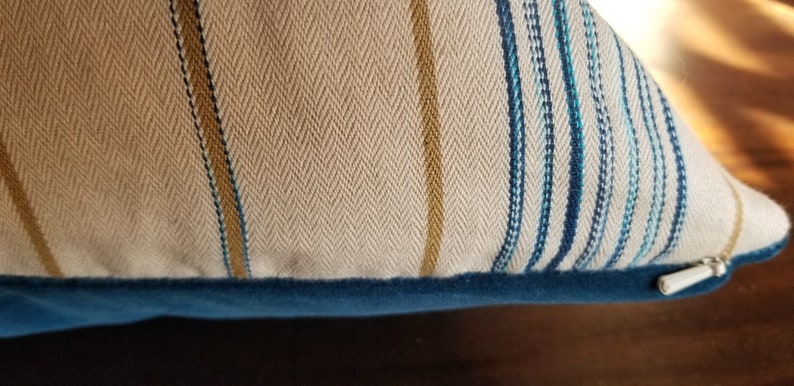 May include: A beige and blue striped throw pillow with a zipper closure and a blue velvet trim.