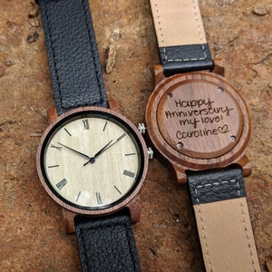 Pu&ograve; includere: Due orologi da polso in legno con cinturini in pelle nera. Un quadrante dell'orologio ha i numeri romani e l'altro ha un messaggio inciso che dice "Happy Anniversary my love! Caroline".