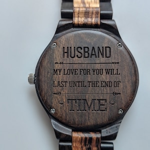 May include: A wooden wristwatch with a dark brown face and a matching wooden band. The watch face is engraved with the word "HUSBAND" above the inscription "MY LOVE FOR YOU WILL LAST UNTIL THE END OF TIME."
