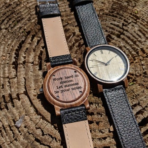 Pu&ograve; includere: Due orologi da polso in legno con cinturini in pelle nera. Un quadrante dell'orologio ha uno sfondo bianco con indici orari romani neri e lancette nere. L'altro quadrante dell'orologio ha uno sfondo in legno con il testo inciso "Lavorare sodo nel silenzio. Lascia che il successo sia il tuo rumore."