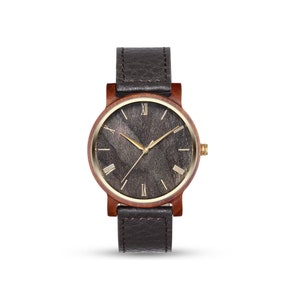 May include: A brown wooden wristwatch with a black leather strap and a gold face with Roman numeral markings.