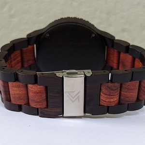 Peut inclure: Un bracelet de montre en bois noir et rouge avec une boucle argent&eacute;e. La boucle porte un petit logo.
