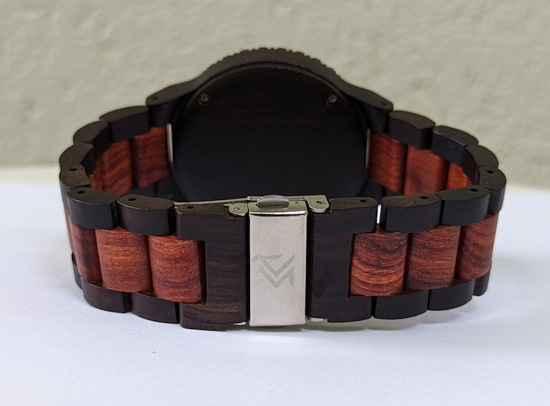Peut inclure: Un bracelet de montre en bois noir et rouge avec une boucle argent&eacute;e. La boucle porte un petit logo.