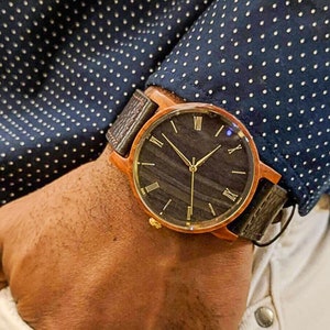 May include: A brown wooden wristwatch with a black face and gold Roman numeral hour markers. The watch has a brown leather strap.