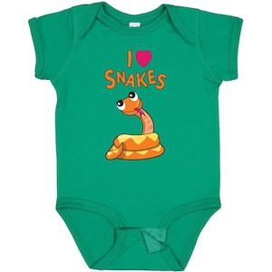 May include: A bright green short-sleeve bodysuit featuring a graphic of a coiled orange snake with large eyes and a pink tongue. Above the snake, the text reads I, followed by a pink heart icon, and the word SNAKES in orange capital letters.