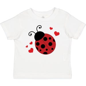 May include: White toddler t-shirt featuring a red ladybug design with black spots and red hearts. The ladybug has a black head and antennae. The graphic is centered on the front of the shirt, creating a playful and cheerful design.