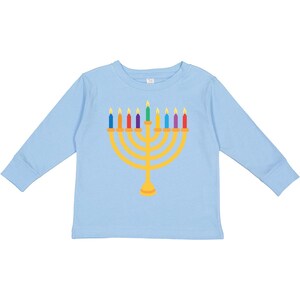 May include: A light blue long-sleeved shirt featuring a gold menorah design with colorful candles. The candles are in shades of blue, red, green, and yellow. The shirt is a comfortable, casual style.