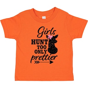 May include: An orange short-sleeved t-shirt featuring a black graphic of a deer silhouette with a pink bow. The text reads Girls HUNT TOO ONLY prettier, accompanied by a black arrow graphic pointing to the right, centered on the front of the shirt.