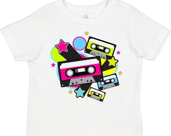 May include: A white short-sleeve t-shirt featuring a graphic print of three cassette tapes in black, pink, lime green, and blue. The design includes colorful circles and stars scattered around the tapes, creating a vibrant, multi-colored pattern on the front of the garment.