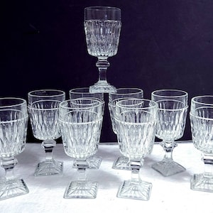 May include: Set of ten clear glass goblets with a square base and a diamond pattern. The goblets are arranged in a pyramid shape.