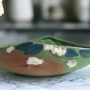 May include: A green ceramic bowl with a leaf design and white flowers. The bowl has a brown glaze and blue accents.