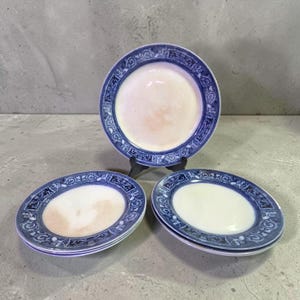 May include: A set of vintage porcelain plates with a white center and a blue decorative border. The plates are oval and round, with a floral and geometric design. The plates are displayed on a gray surface.
