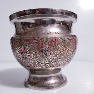 May include: A silver vase with an ornate floral design in shades of red, gold, and green. The vase has a round body and a flared lip.