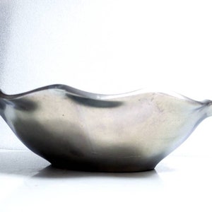 Peut inclure: Un bol en c&eacute;ramique ondul&eacute; de couleur argent&eacute;e avec une surface lisse et r&eacute;fl&eacute;chissante.