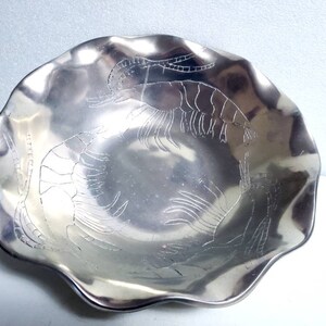 Peut inclure: Un bol en argent avec un bord festonn&eacute; et un motif en relief de crevettes. Le bol est en m&eacute;tal et a une finition brillante.