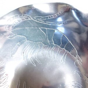 Peut inclure: Un bol en m&eacute;tal argent&eacute; avec un motif grav&eacute; de crevettes. Le bol a un bord ondul&eacute; et une finition brillante.