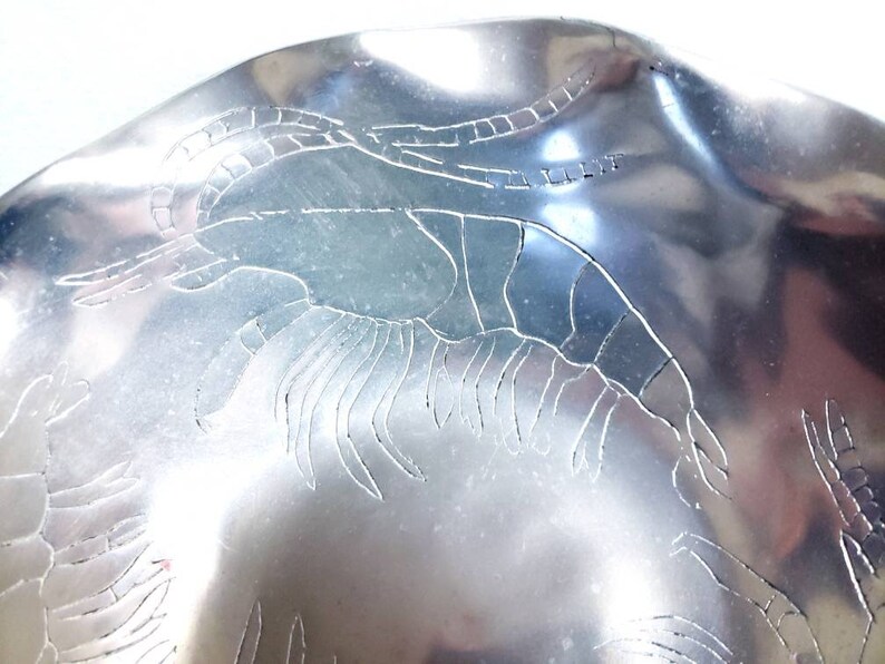 Peut inclure: Un bol en m&eacute;tal argent&eacute; avec un motif grav&eacute; de crevettes. Le bol a un bord ondul&eacute; et une finition brillante.
