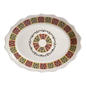 May include: Oval serving platter with a scalloped edge. The white ceramic dish features a repeating pattern of orange, green, and brown geometric shapes around the rim and a central circular design.