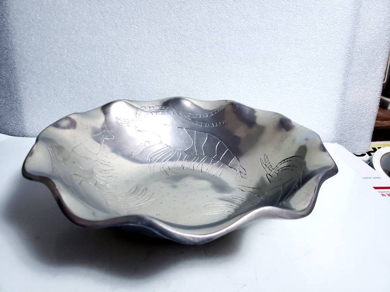 Peut inclure: Un bol de service en argent avec un bord festonn&eacute; et un motif de crevettes en relief. Le bol est en m&eacute;tal et a une finition brillante.