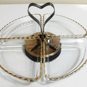 May include: A four-section glass serving dish with a gold rim and a heart-shaped metal handle. The dish is on a wooden base.