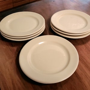May include: A set of four white ceramic plates, stacked on top of each other. The plates are round and have a slightly raised rim.