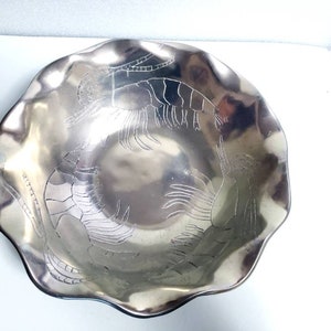 Peut inclure: Un bol de service en argent avec un bord festonn&eacute; et un motif en relief de deux crevettes. Le bol est en m&eacute;tal et a une finition brillante.