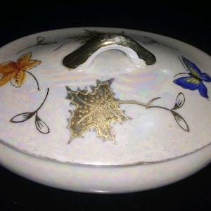 May include: A white porcelain serving dish with a lid. The lid has a gold handle and a butterfly design. The dish is decorated with gold leaf and floral designs.
