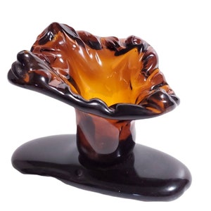 May include: A brown glass vase with a unique, organic shape. The vase has a wide, open top and a narrow base. The base is a separate piece and is black.