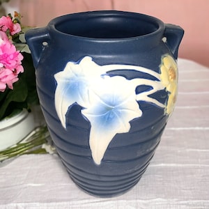 May include: A blue ceramic vase with white and yellow floral designs. The vase has two handles and a ribbed texture.