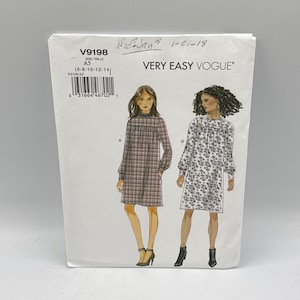 May include: A Very Easy Vogue V9198 sewing pattern envelope for sizes 6-8-10-12-14. The white paper envelope features illustrations of two knee-length dresses with long sleeves and gathered necklines, one in a plaid print and one in a floral print.